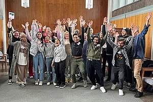 Gruppenbild von Schülerinnen und Schülern, die freudig die Arme heben und in die Kamera lächelnd